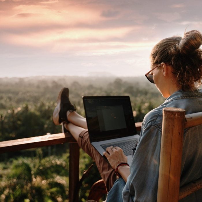 Young business woman working at the computer in cafe on the rock. Young girl downshifter working at a laptop at sunset or sunrise on the top of the mountain to the sea, working day.